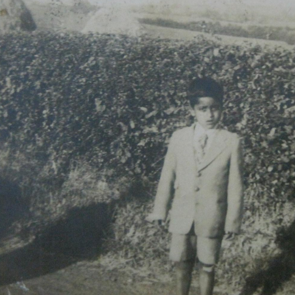 Black and white photo of an Indian child wearing a suit with shorts and standing in a house garden